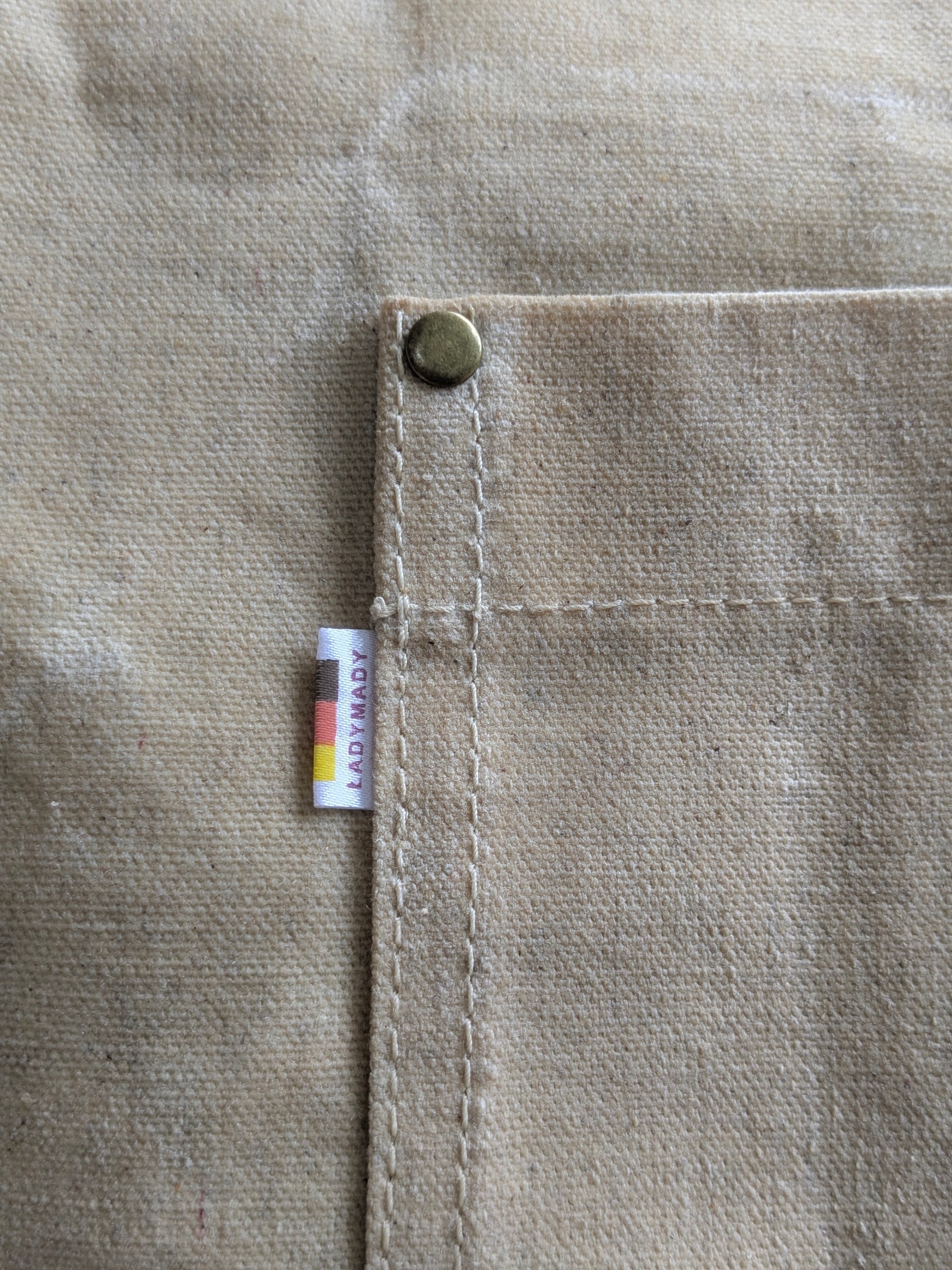 Close-up of LadyMady Handmade Waxed Canvas Tote Bag showcasing the durable stitching and brass button on the pocket. Waxed canvas tote bag.